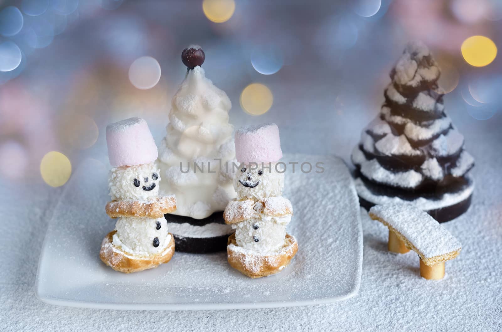 Little cakes snowmen and chocolate trees in powdered sugar. On the background of colorful bokeh. by Gaina