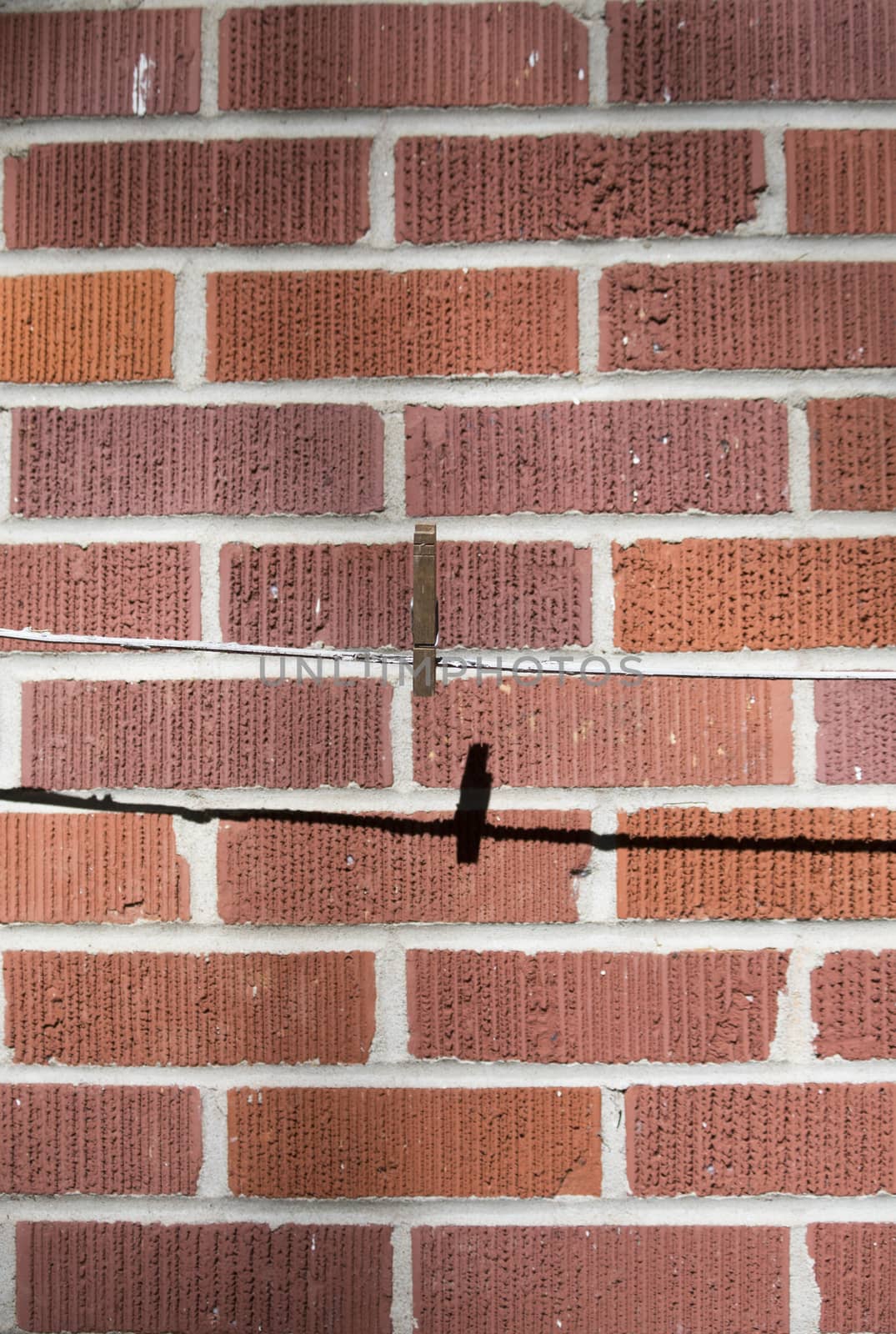 Vertical image of single clothes pin on a laundry line against a red brick wall