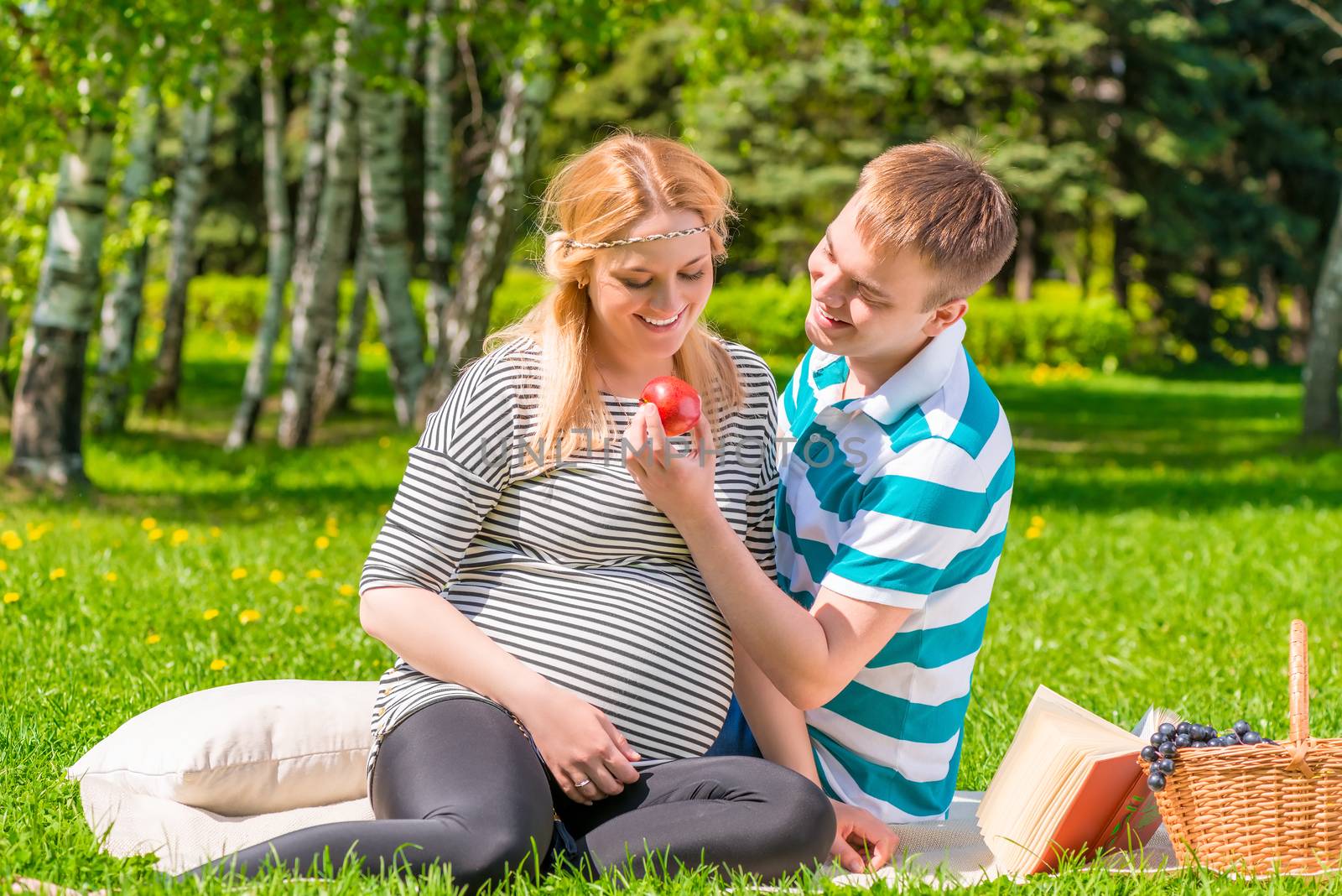 Portrait of a happy pregnant couple at a picnic with apple