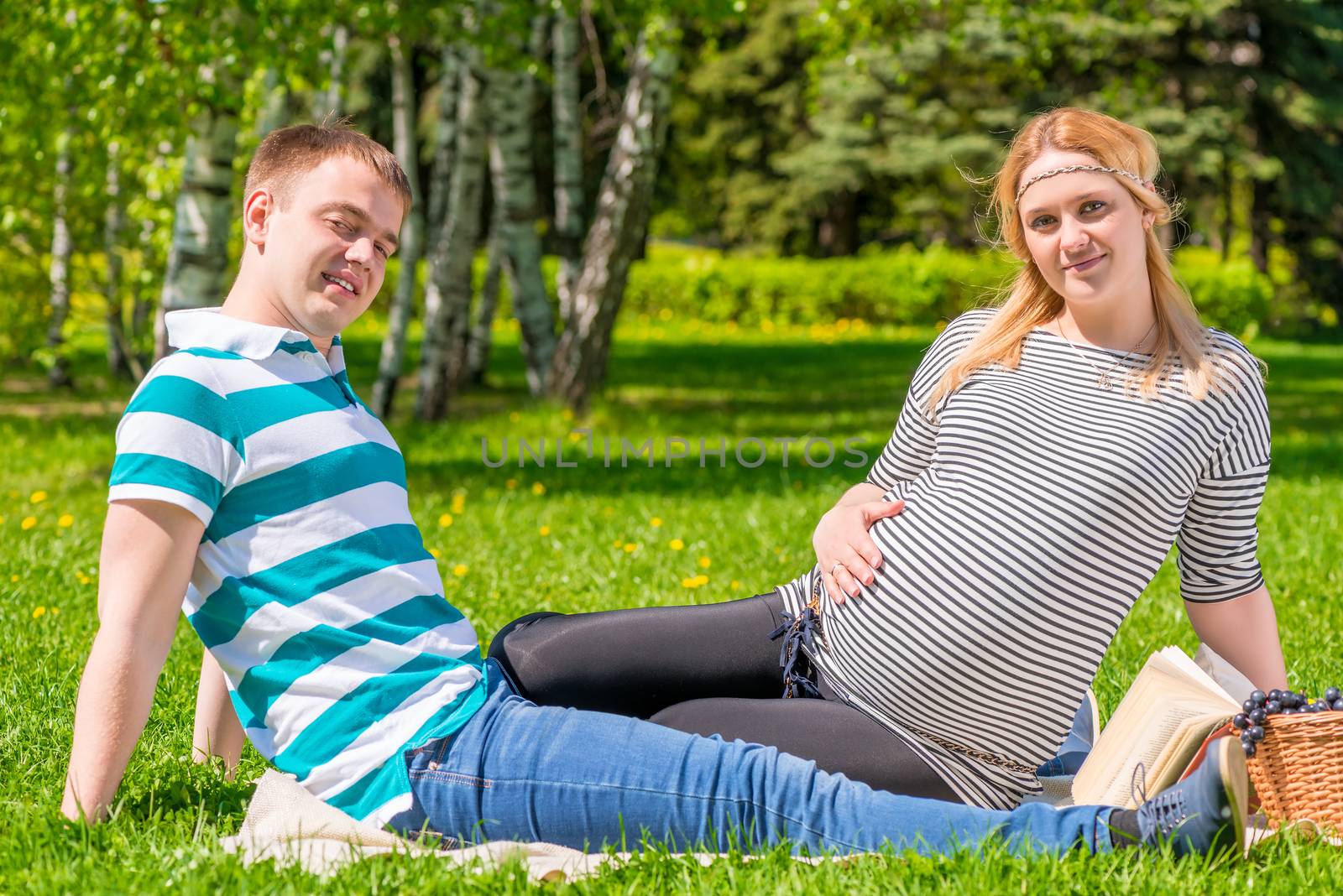 couple waiting for baby sitting in the park with a basket of fruit on a picnic
