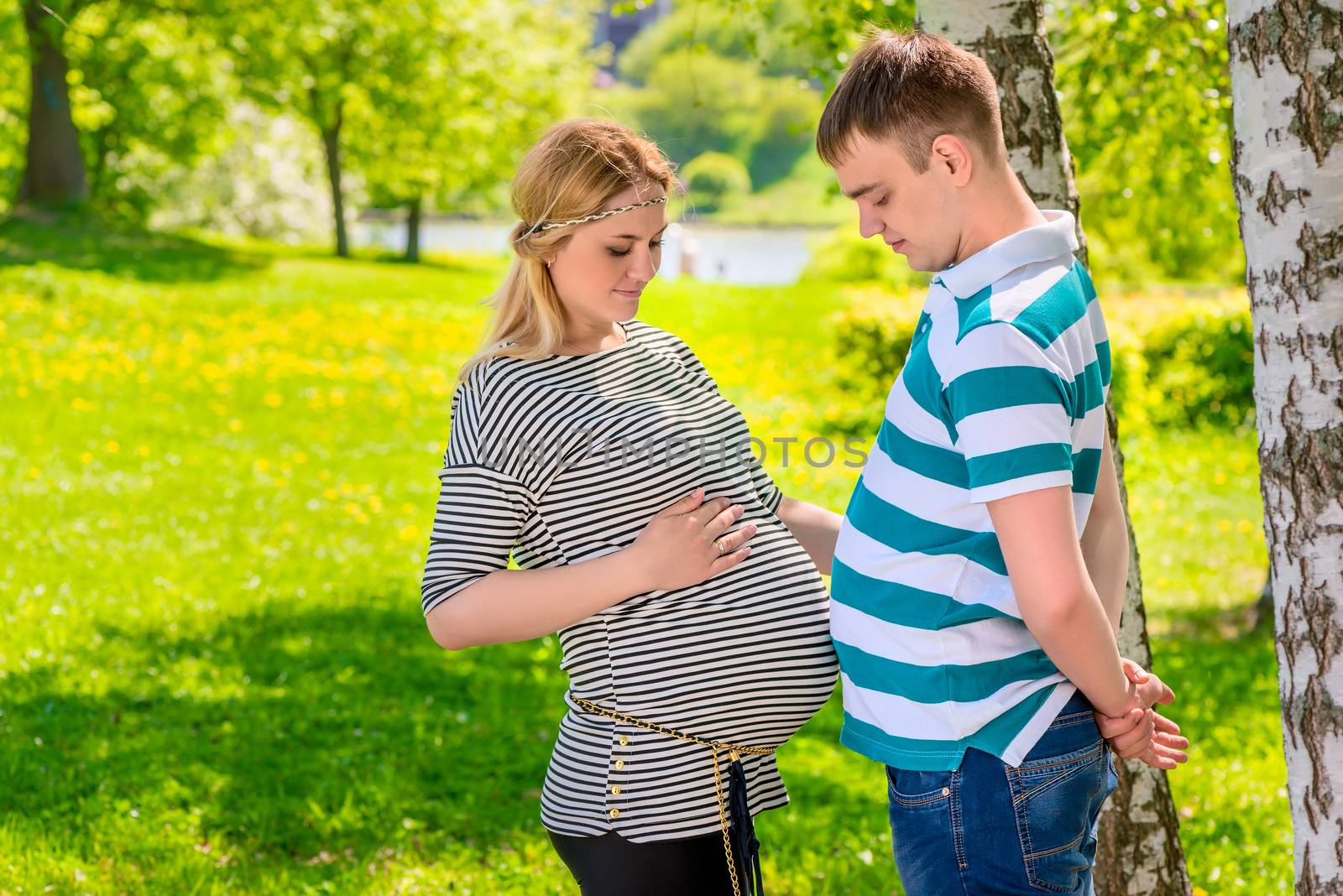 man and pregnant woman compare their stomachs, shot in the park summer day