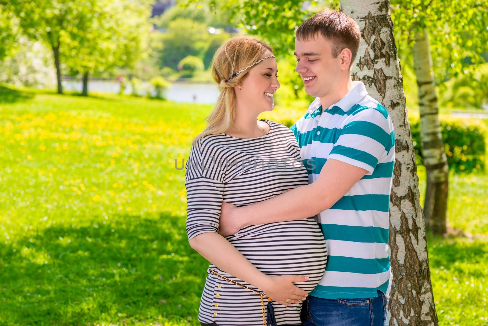 young man embracing his beautiful pregnant wife in the park