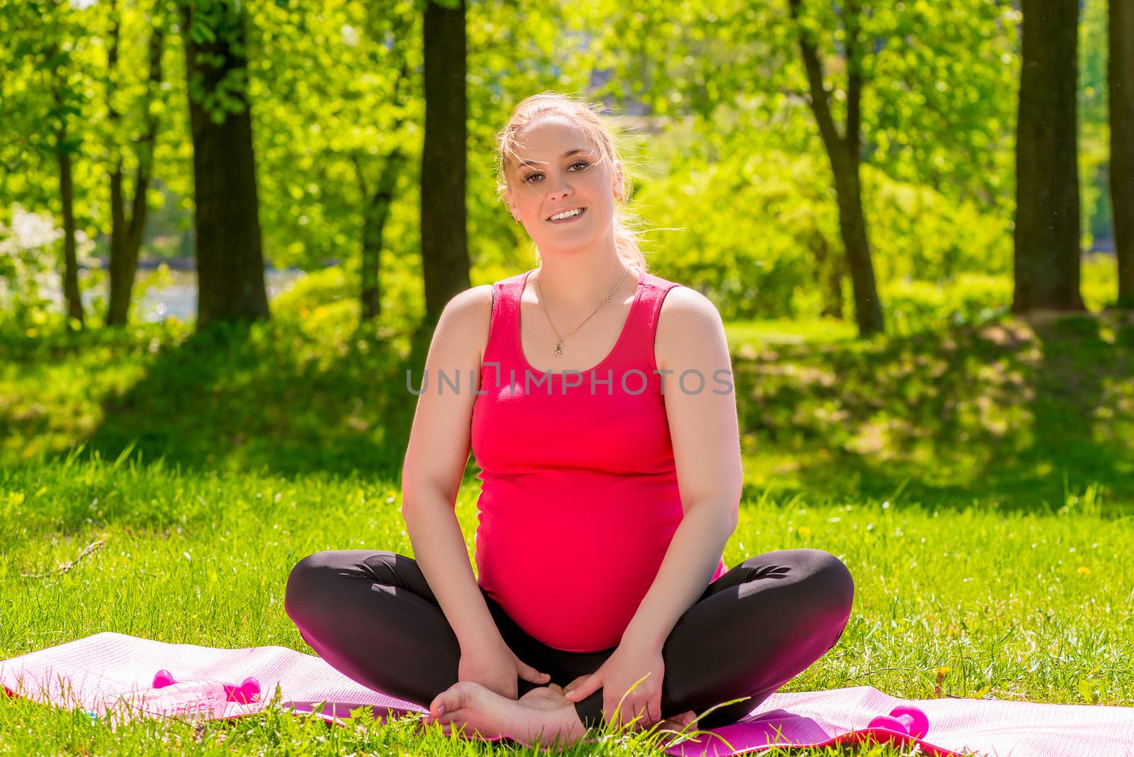 beautiful young pregnant woman in the park on a mat doing yoga by kosmsos111