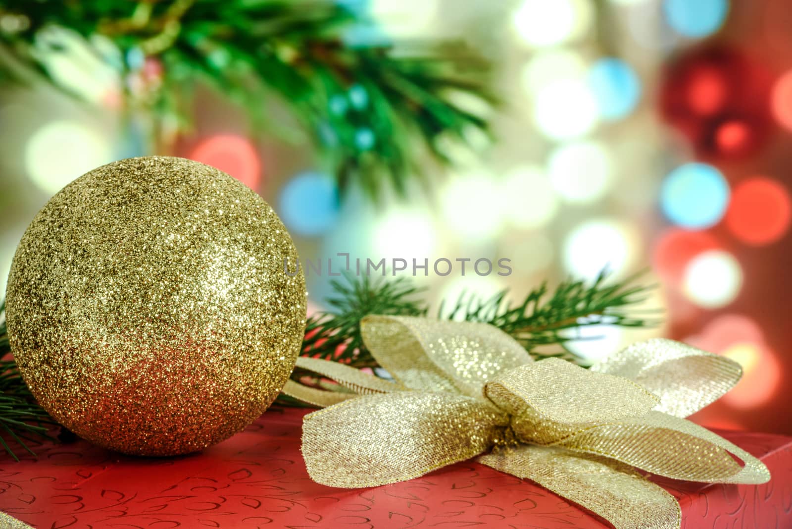 Red gift with a beautiful gold ribbon and a bauble on the background of colored Christmas decorations