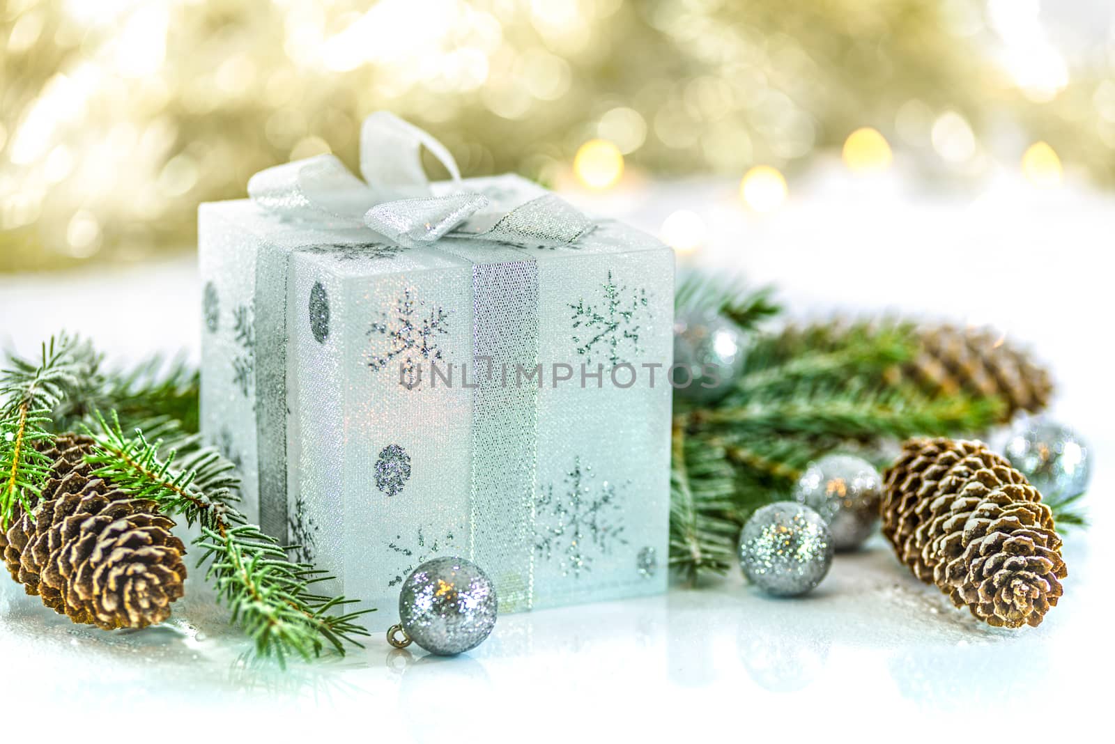 Silver and white gift with spruce twigs and cones in the background lights