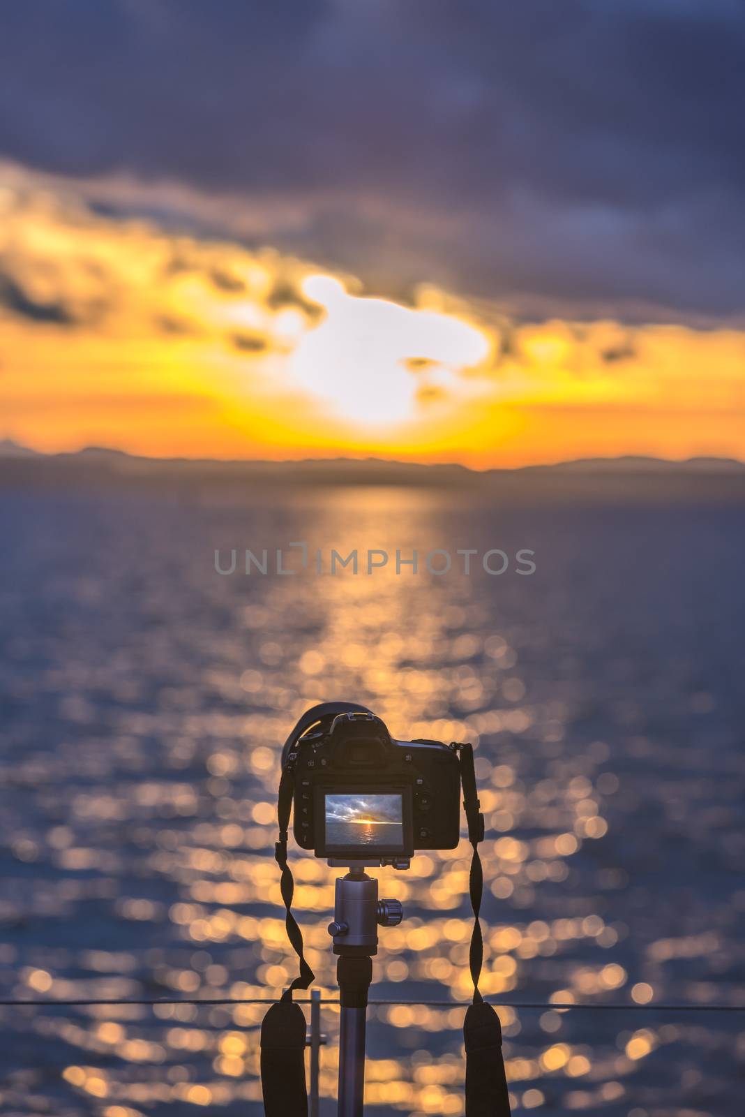 Colorful image with a DSLR camera on a tripod capturing, in live view mode, a beautiful sunset over the water.