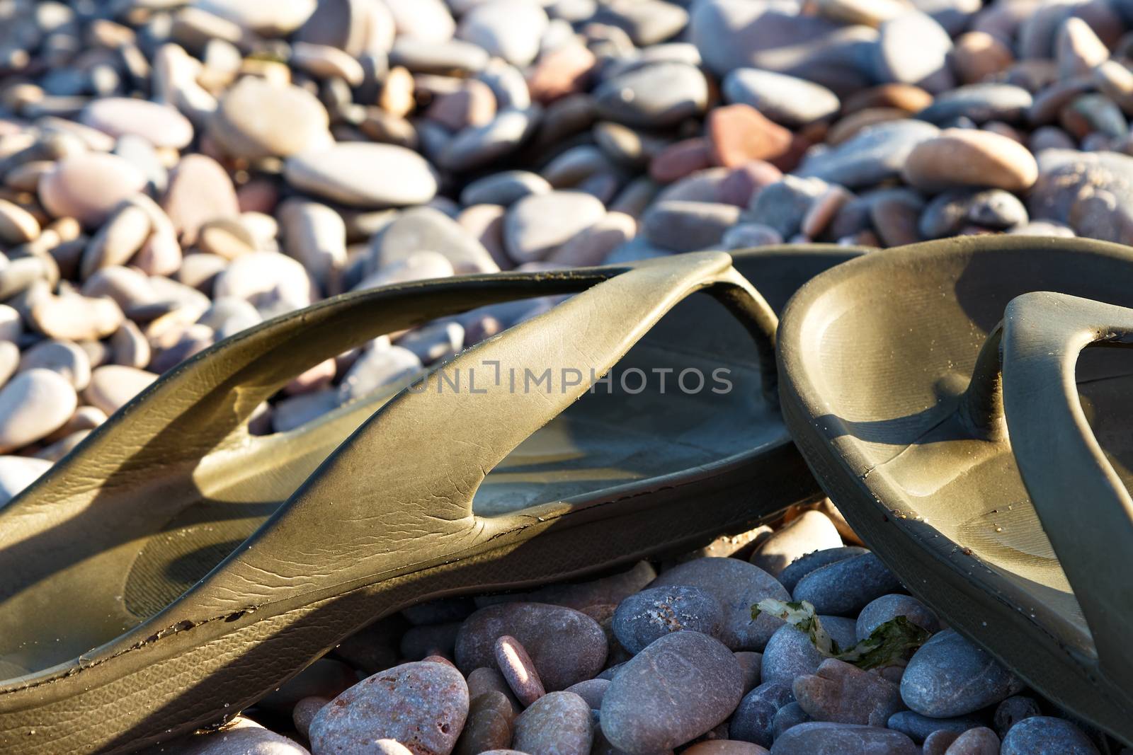 Green Flip Flops on a stones beach. Horizontal image.