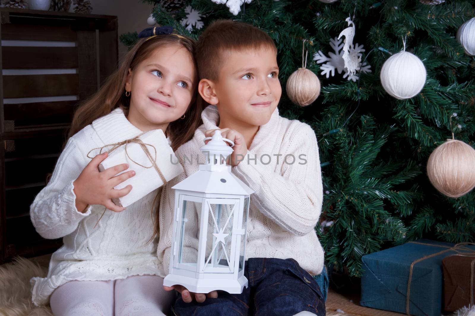 Sister and brother sittting together and looking aside under Christmas tree