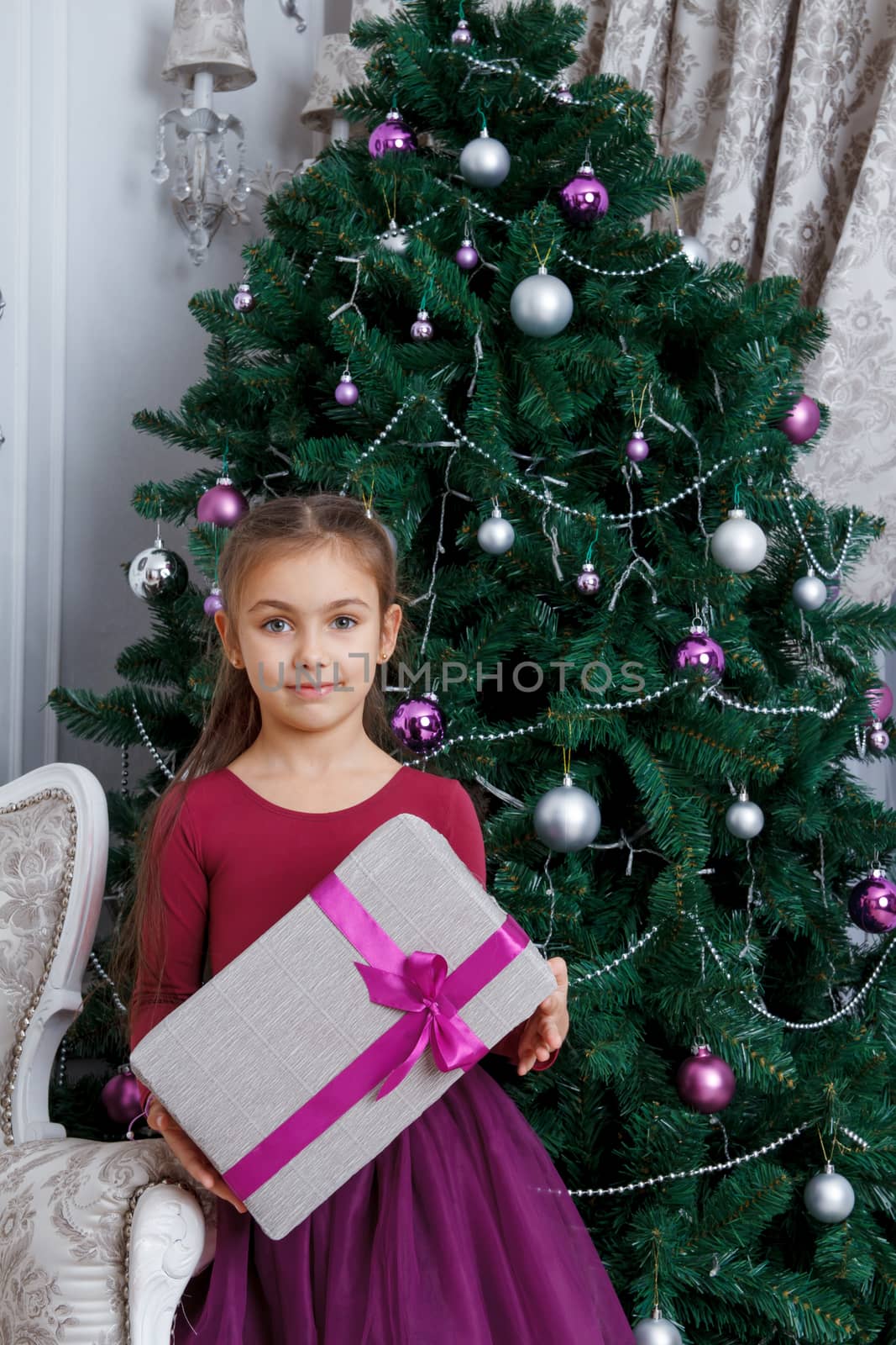 Pretty girl holding magenta gift-box under christmas tree