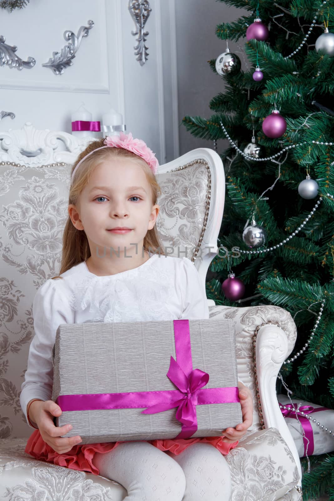 Pretty girl holding gift-box sitting under Christmas tree