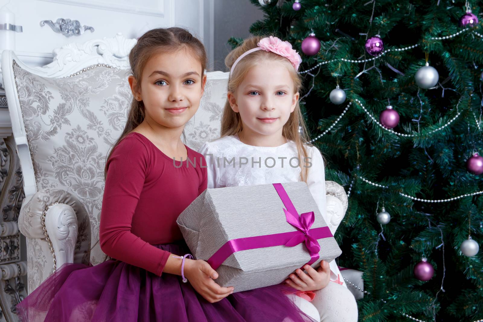 Girls holding big gift-box under Christmas tree by Angel_a