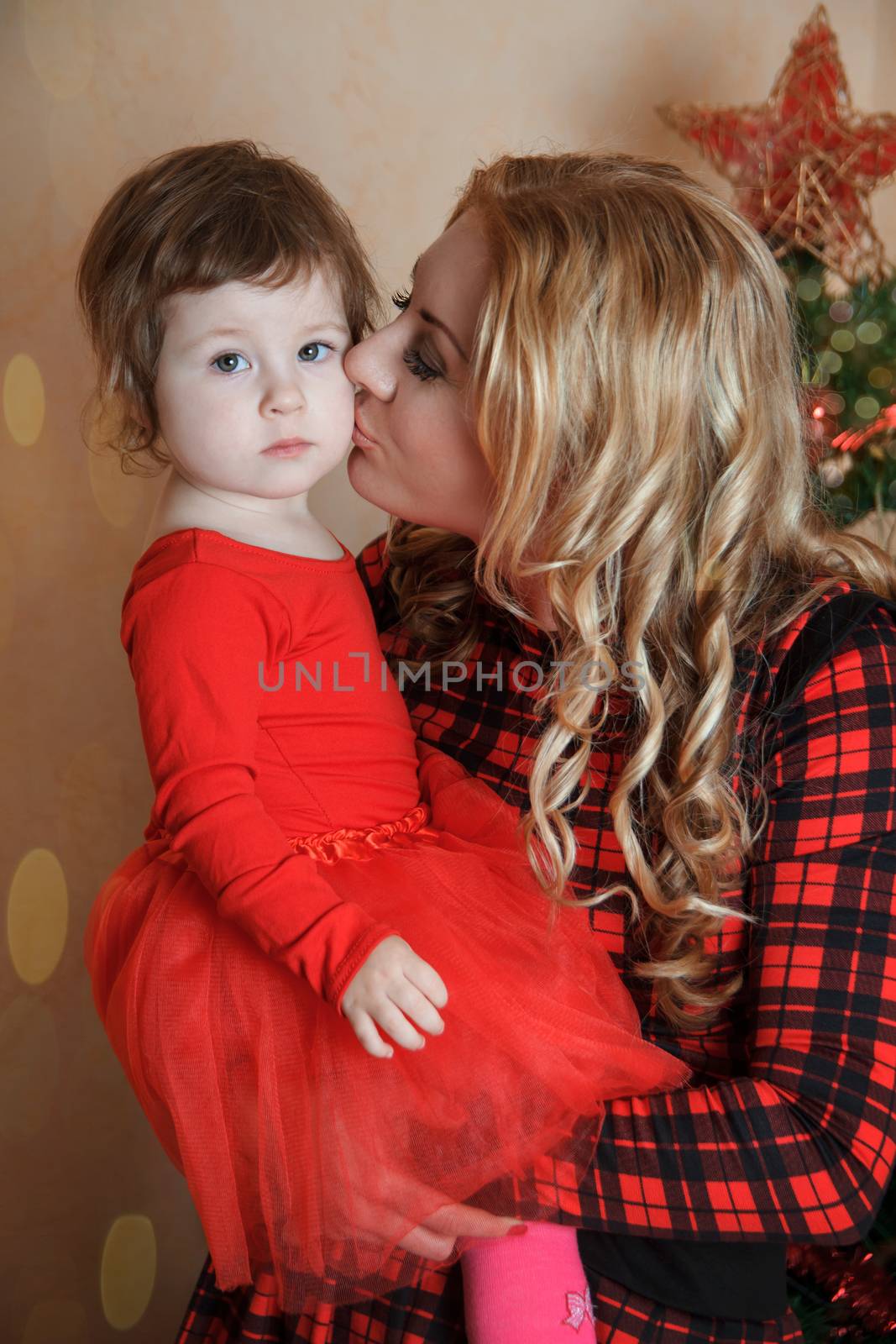 Mother kissing small daughter under Christmas tree