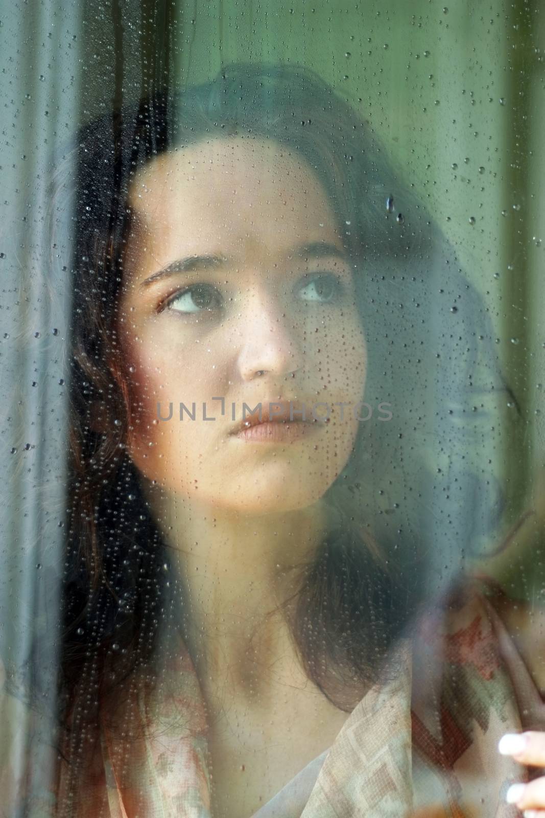 Woman with sad smile behind a wet window