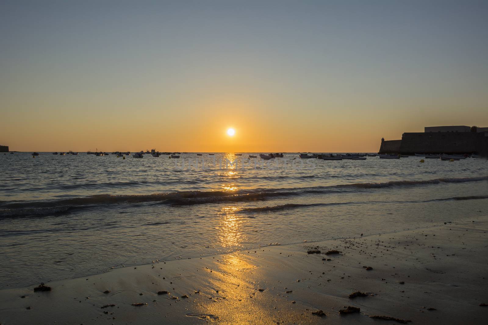 Beautiful sunset on a beach with fishing boats at the bottom, Caleta beach, Cadiz, Spain