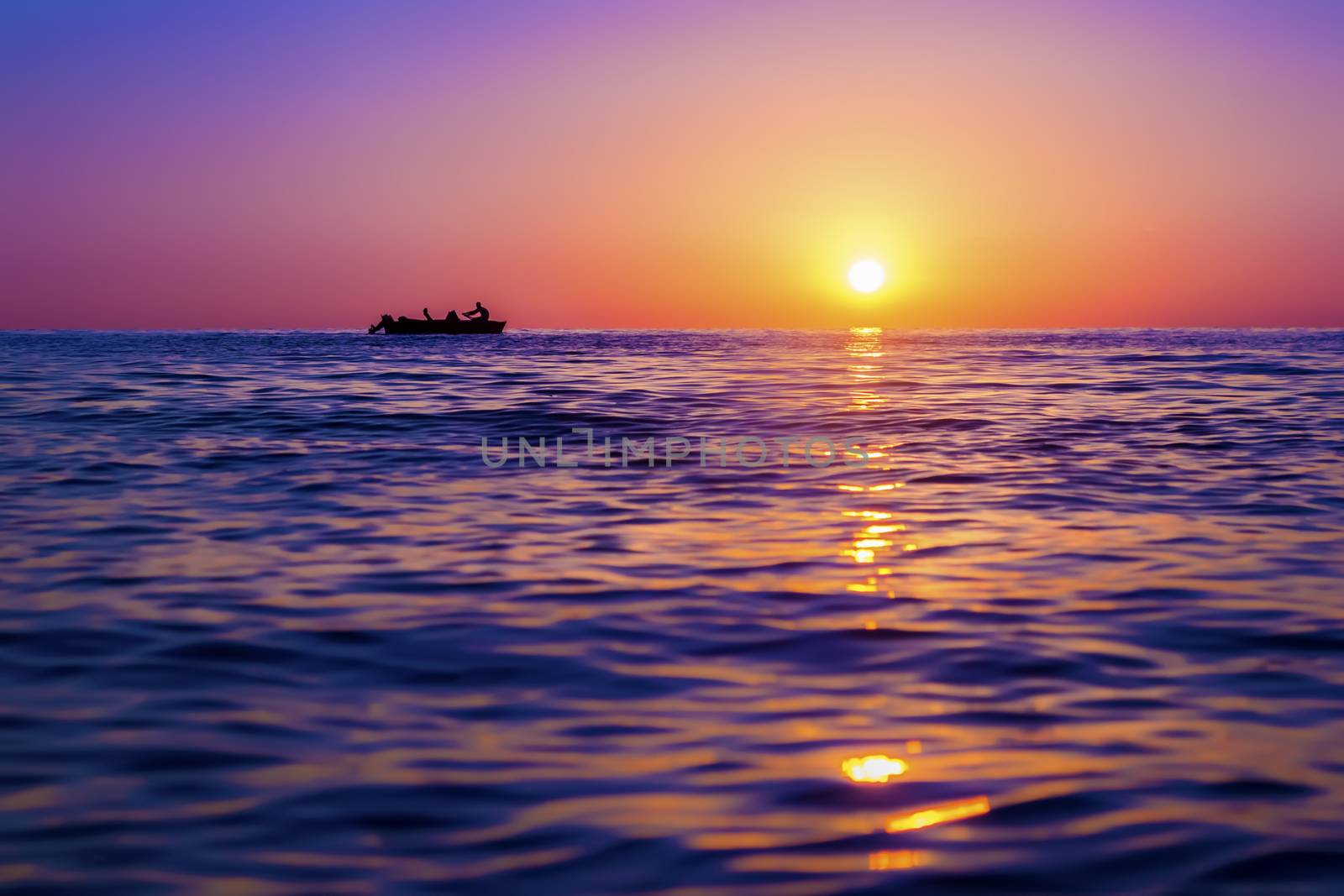Evening seascape. Silhouette of man on the row boat against the setting sun. The sun reflected off the waves. Purple, pink and yellow colors. Georgia