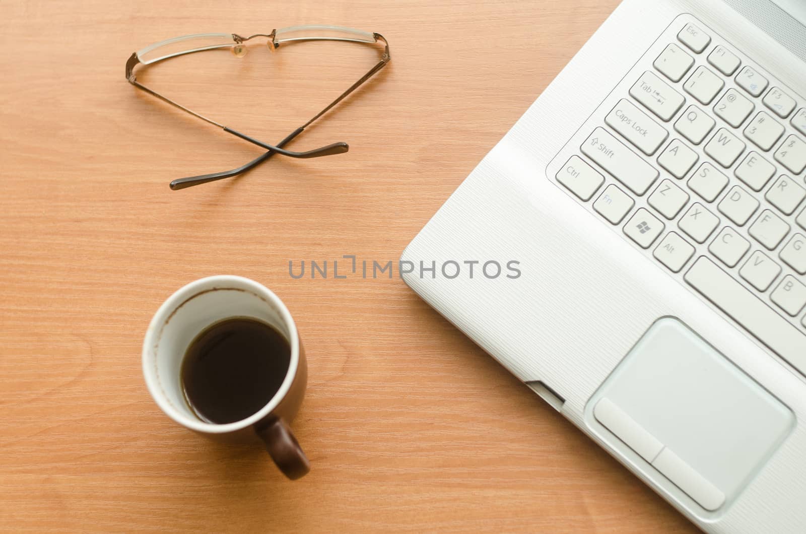 On the table is a laptop, a cup of coffee and glasses, view from above