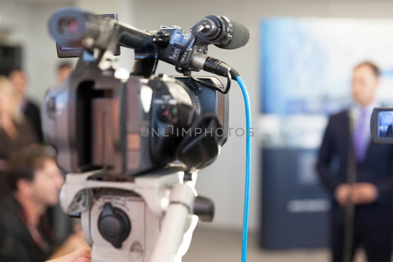 Video camera in focus, blurred spokesperson in background by wellphoto