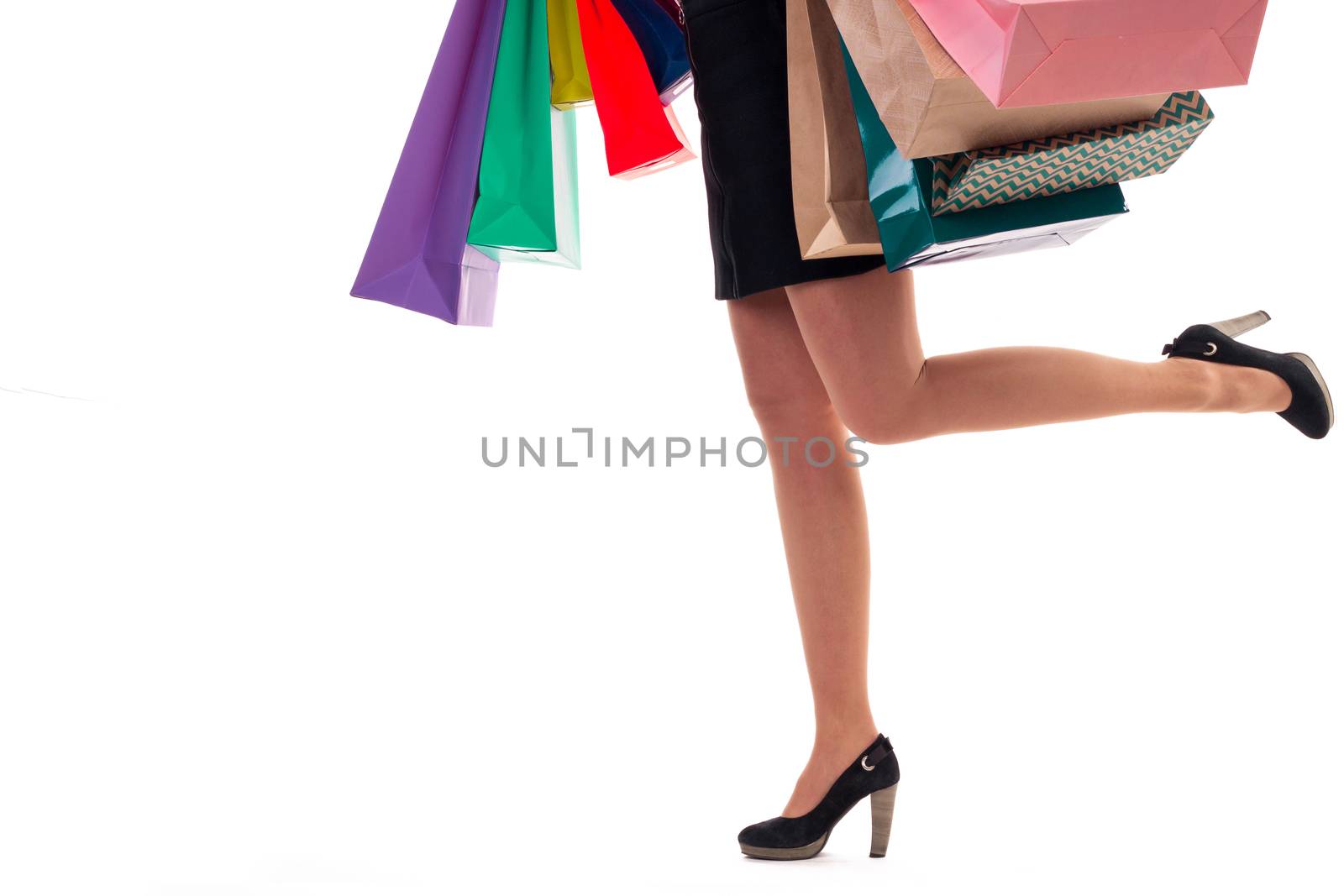 Lower close-up of running woman wearing short skirt and shoes with high hills holding multicolored shopping paper bags and packages, isolated on white background