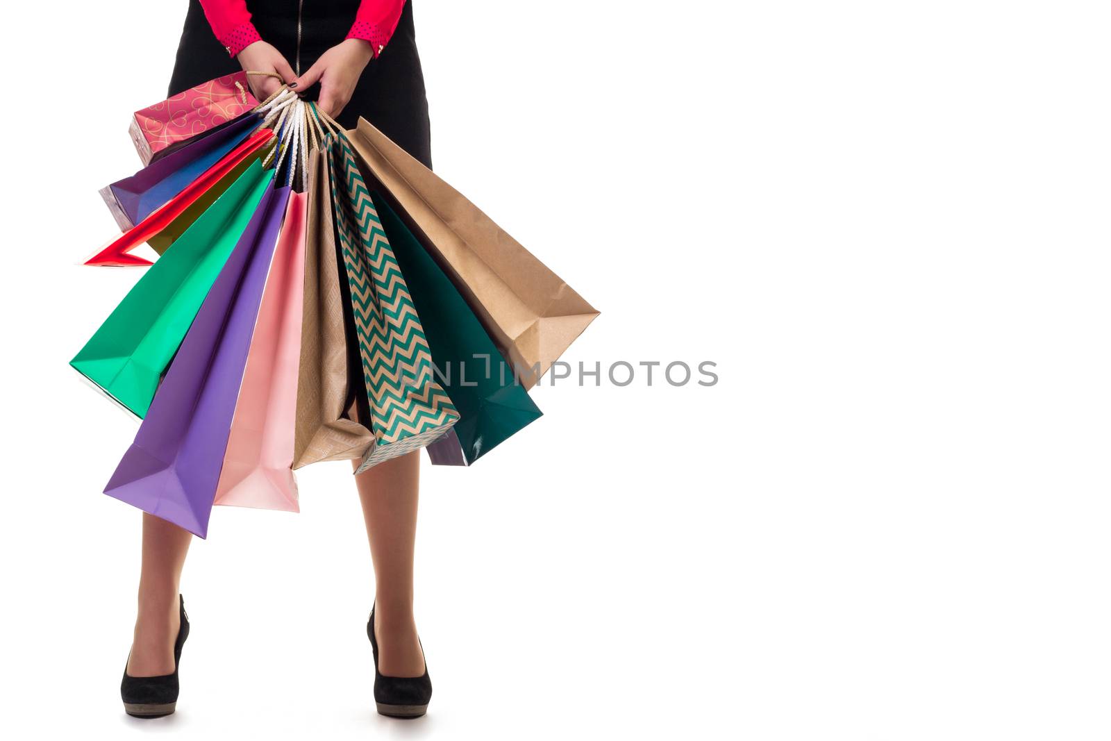 Lower close-up of standing woman wearing short skirt and shoes with high hills holding multicolored shopping paper bags and packages, isolated on white background