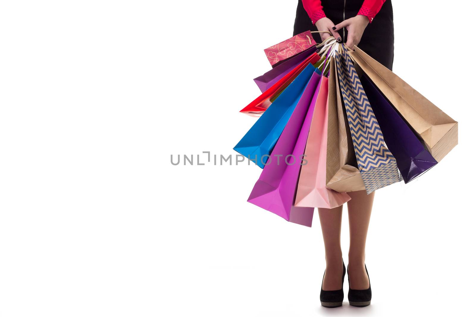 Lower close-up of standing woman wearing short skirt and shoes with high hills holding multicolored shopping paper bags and packages, isolated on white background
