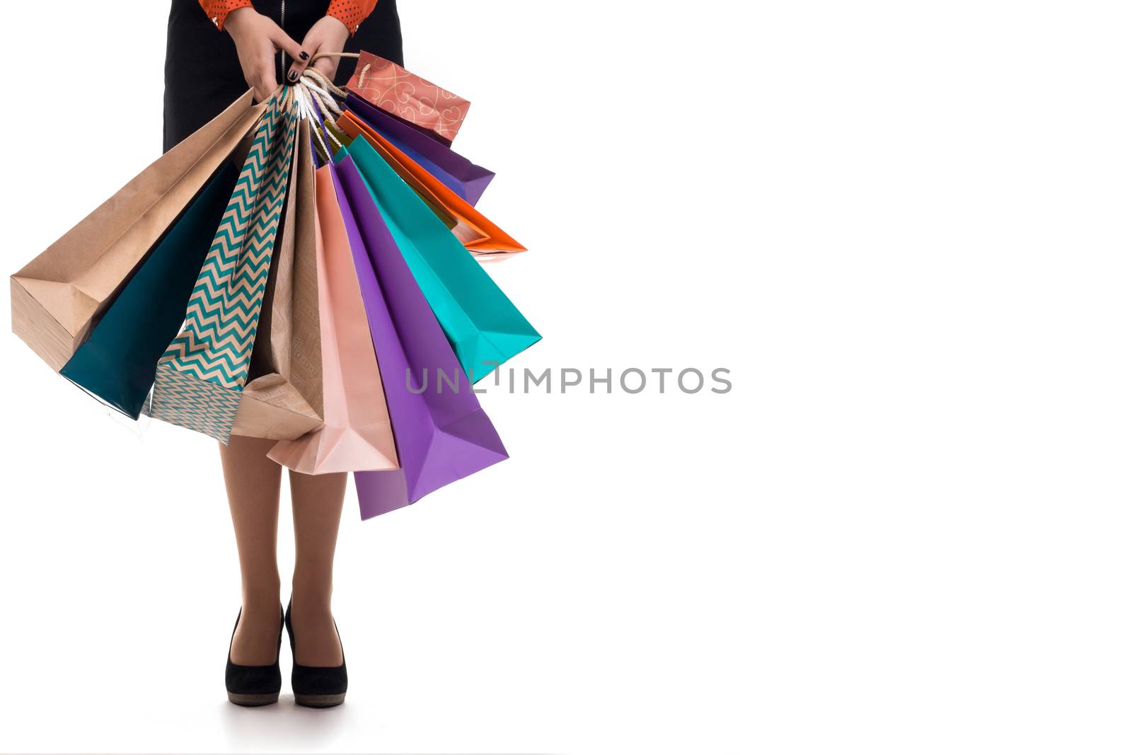 Lower close-up of standing woman wearing short skirt and shoes with high hills holding multicolored shopping paper bags and packages, isolated on white background