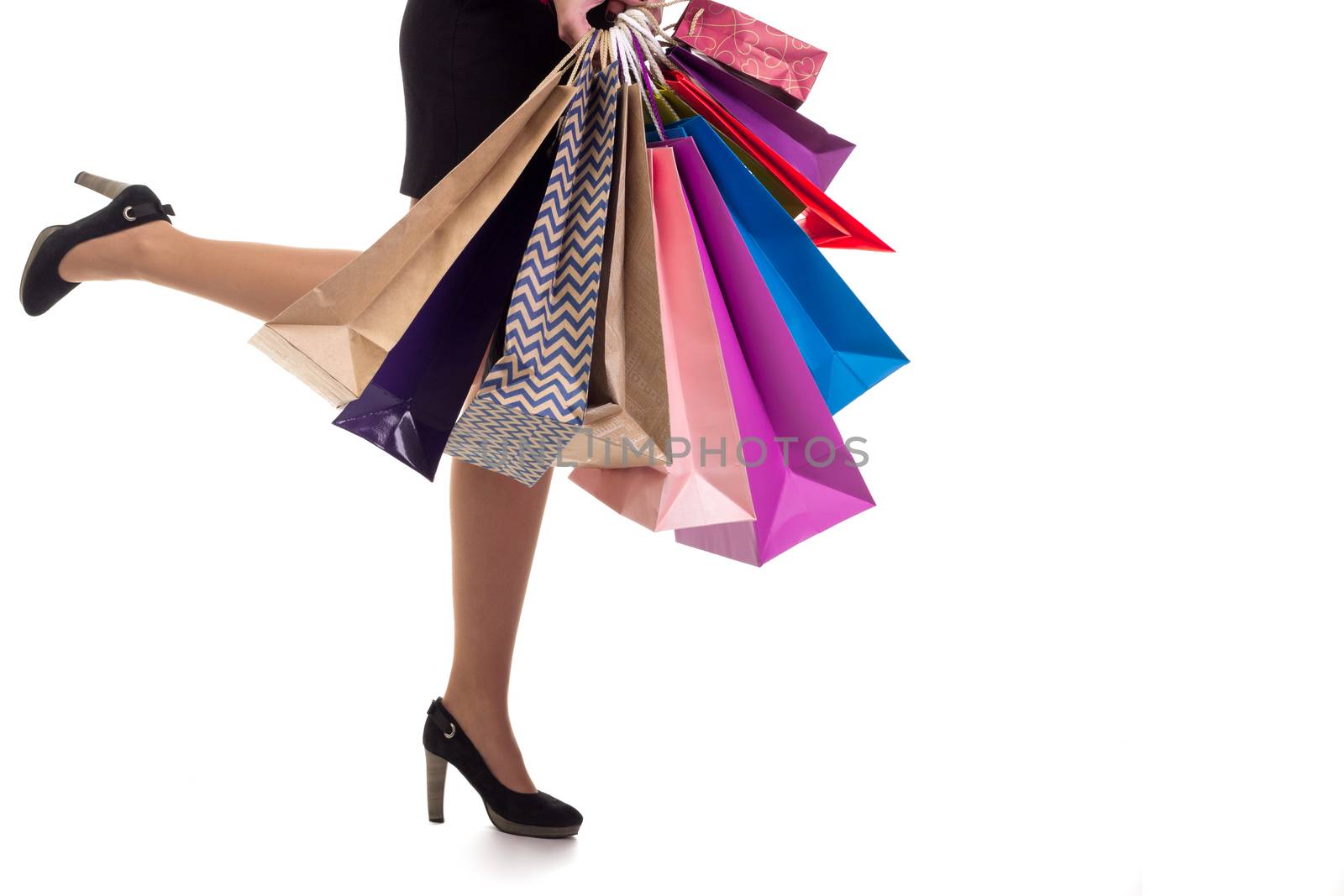 Lower close-up of running woman wearing short skirt and shoes with high hills holding multicolored shopping paper bags and packages, isolated on white background