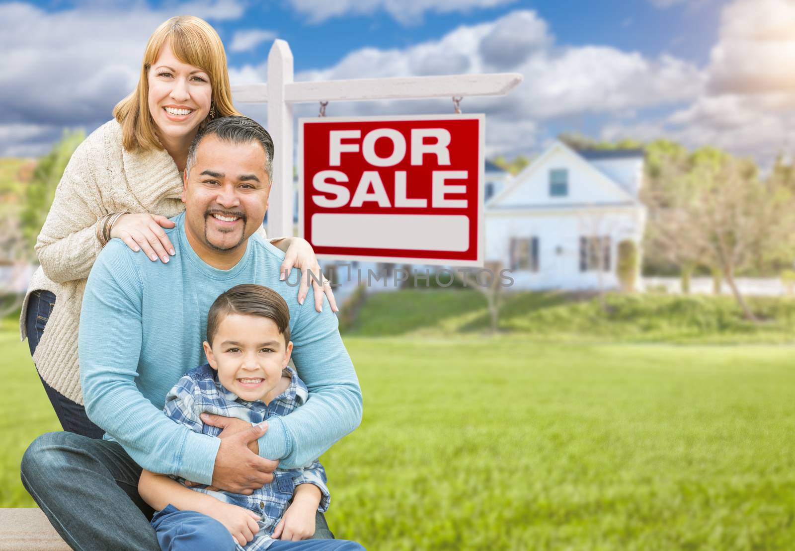 Happy Mixed Race Hispanic and Caucasian Family Portrait In Front of House and Sold For Sale Real Estate Sign.
