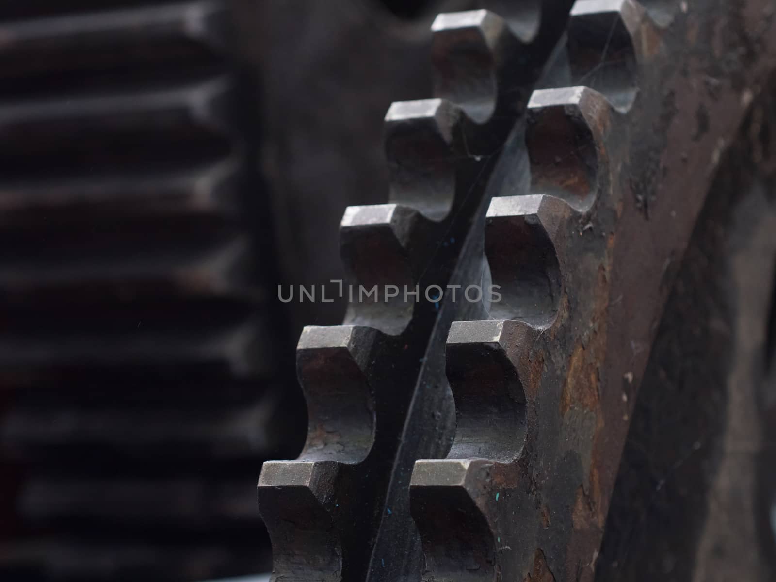 Detail of old, rusty cogwheel in industrial environment. Very shallow depth of field with only the nearest teeth in focus.