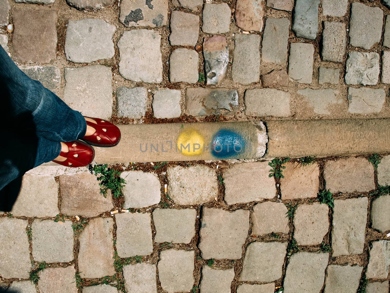 Legs and feet of a woman standing on the stone floor. Woman wearing blue jeans, red sneakers and standing near yellow and blue spots