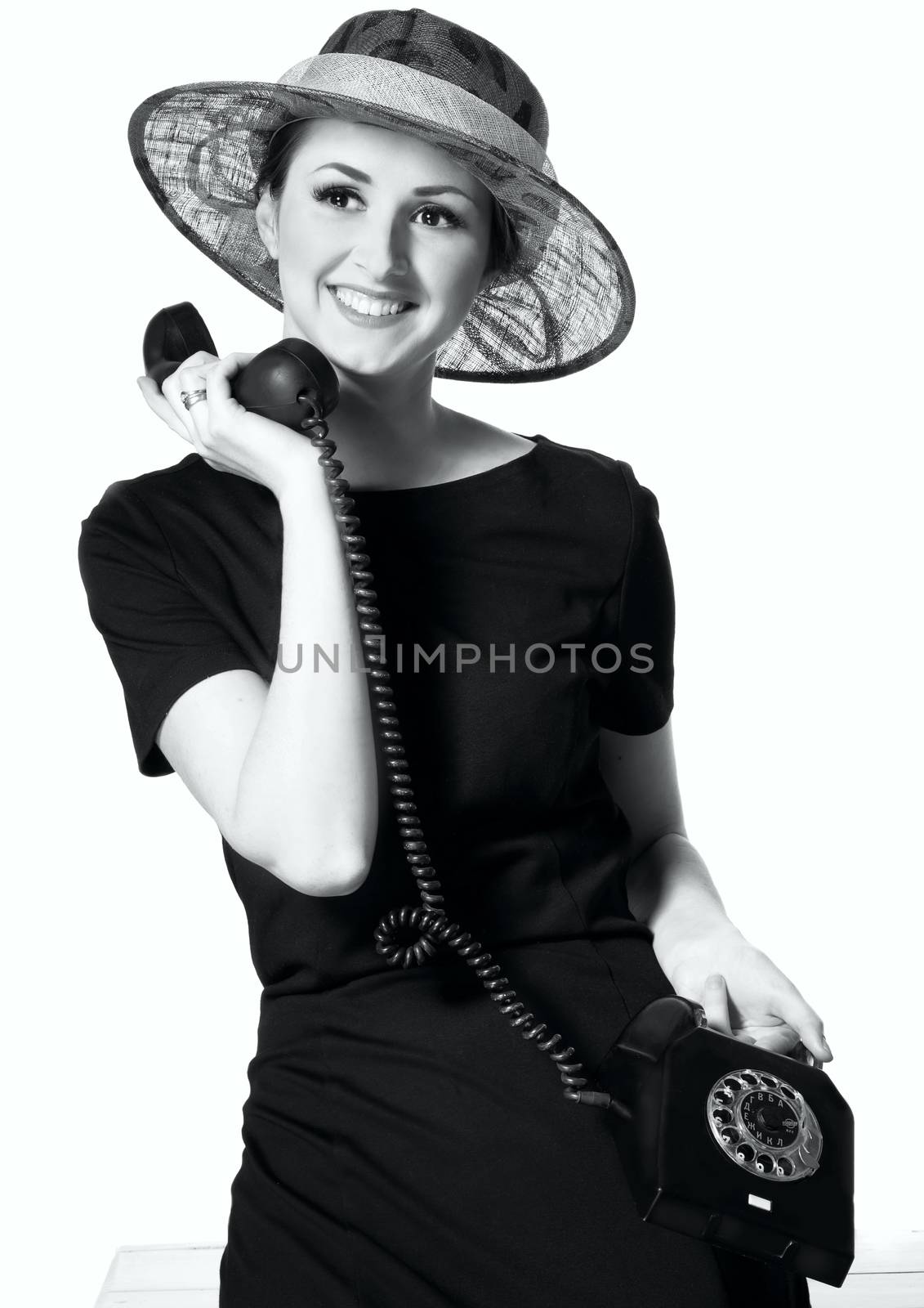 Portrait of a beautiful brown-eyed woman in a little black dress with a vintage telephone isolated on white background