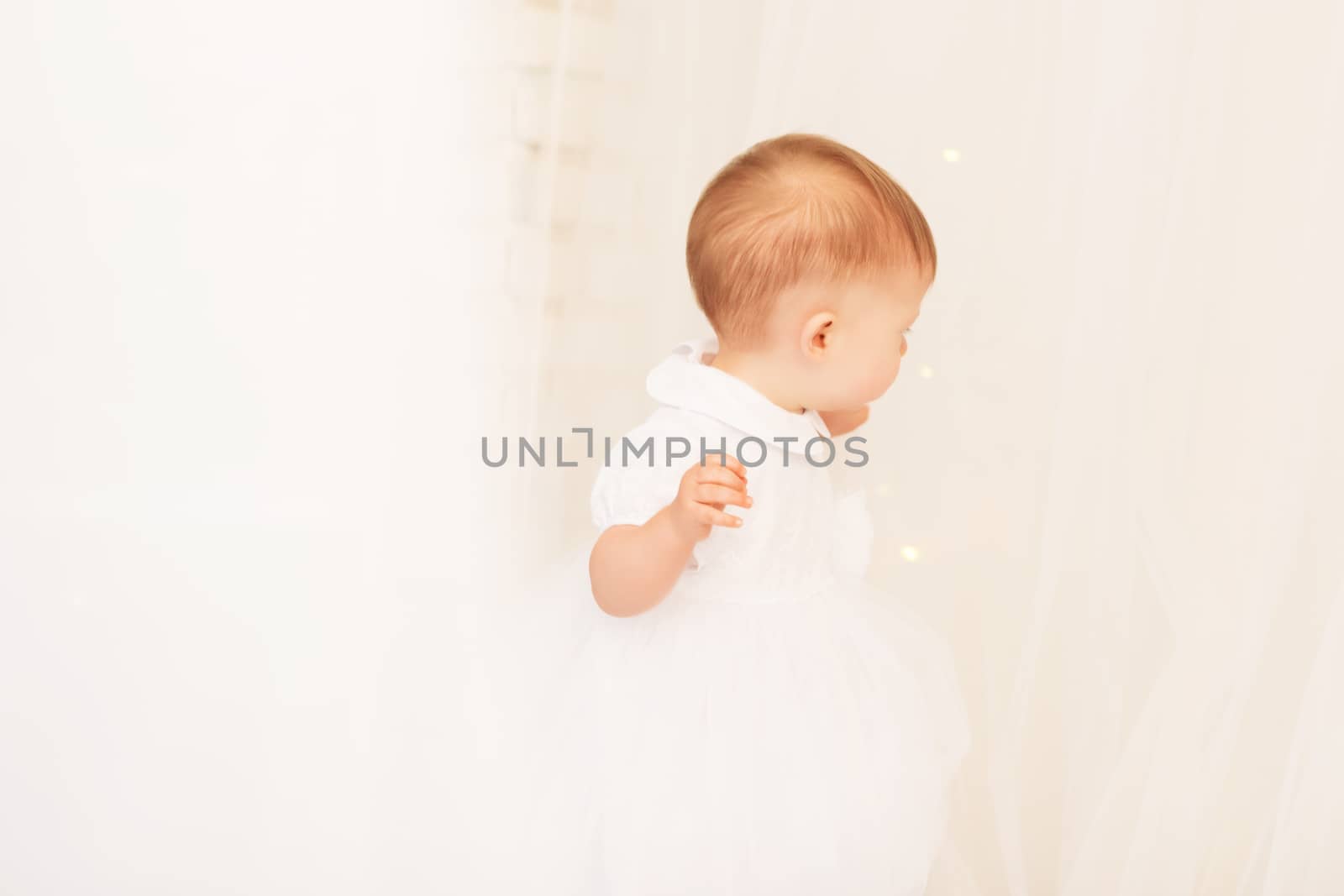 Portrait of a beautiful baby girl in a white dress in the interior with Christmas decorations