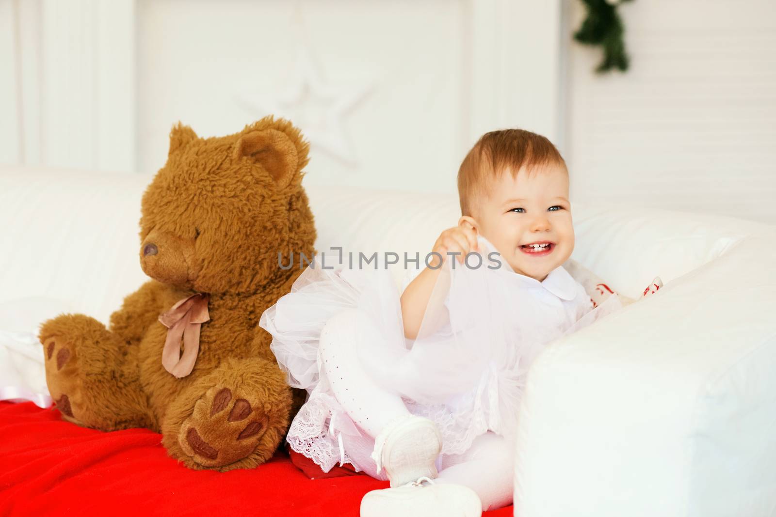 Portrait of a beautiful baby girl with a soft brown teddy bear in the interior with Christmas decorations.