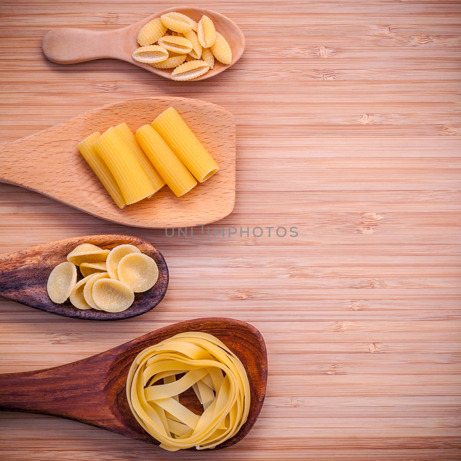 Italian foods concept and menu design . Various kind of Pasta Fettucini ,Rigatoni ,Rigatoni and Gnocco Sardo in wooden spoons setup on bamboo cutting board with flat lay.