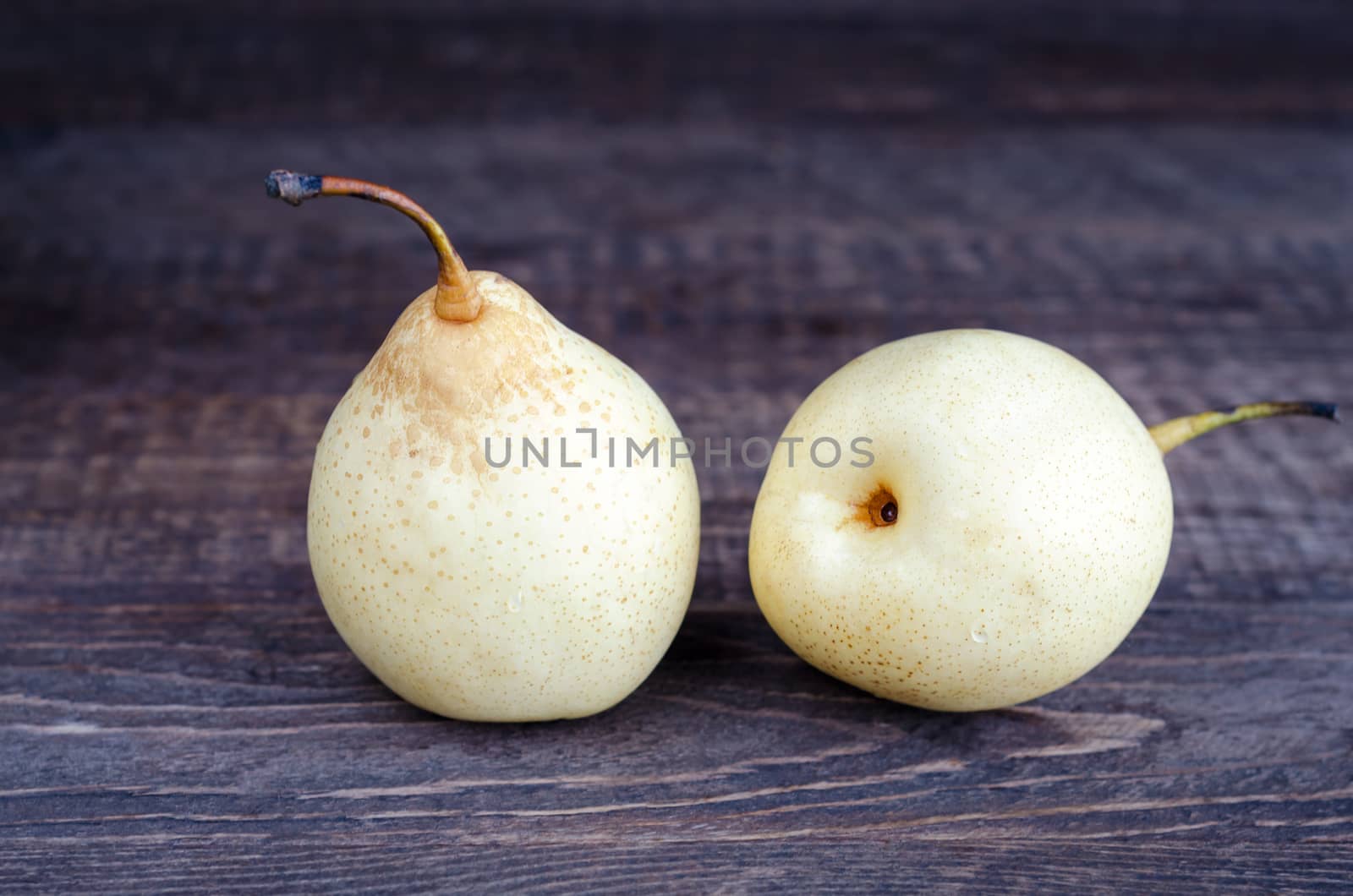 Two yellow pear lying on a wooden surface. Selective focus, low key.
