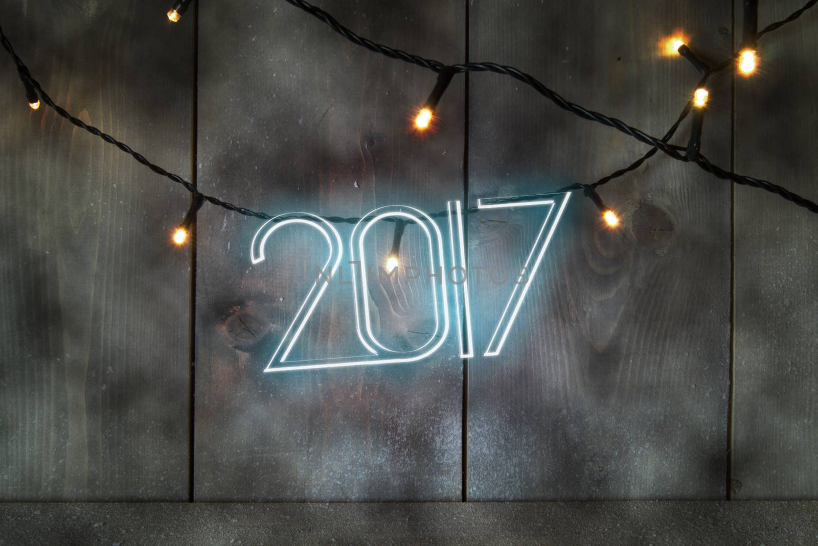 Neon text spelling 2017 on a wooden background with festive lights