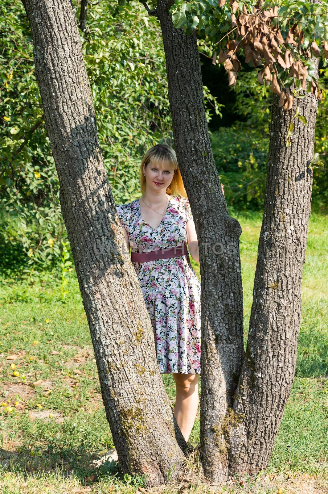 Pregnant woman stands between the trees in Park Sunny summer day.