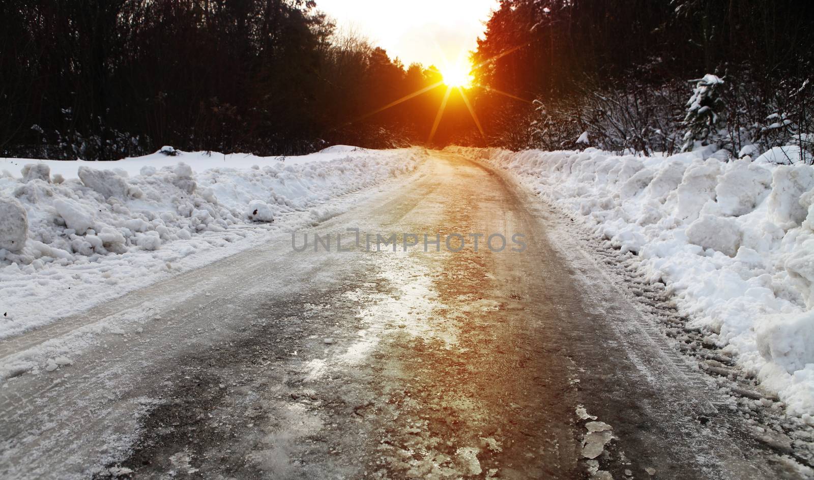 Snow covered winter road with shining streetlights in rural areas at sunset