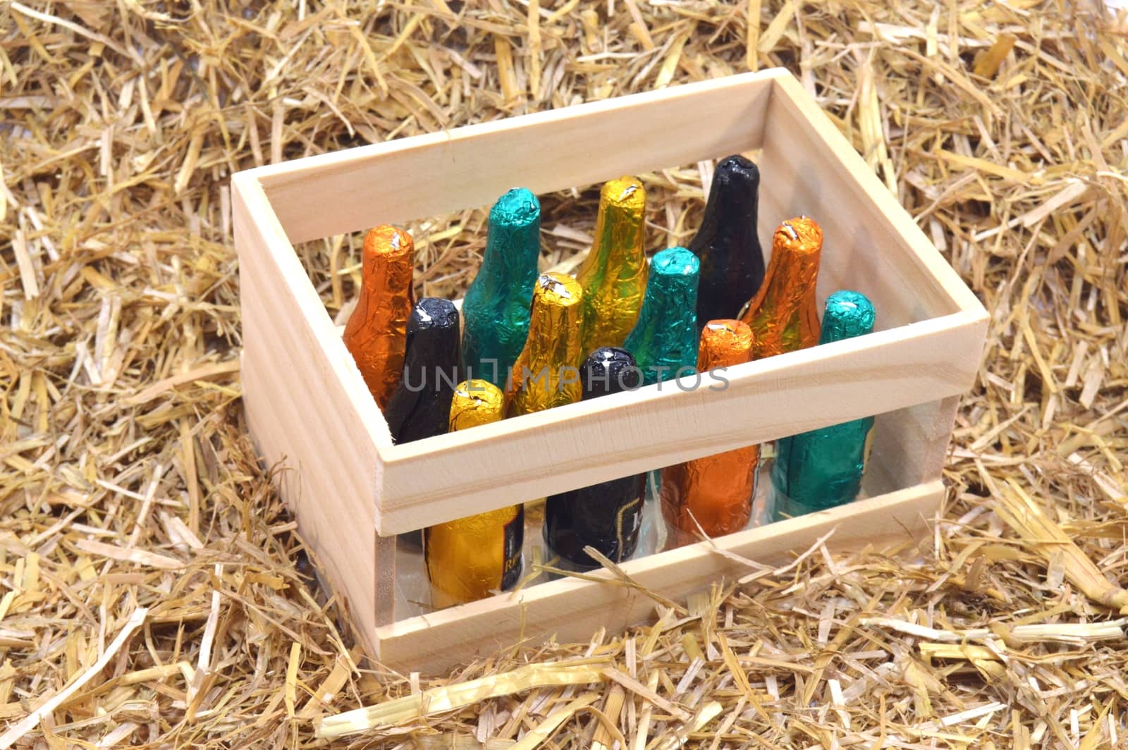 Wooden box of twelve bottles of chocolate filled with liqueur on a background of straw