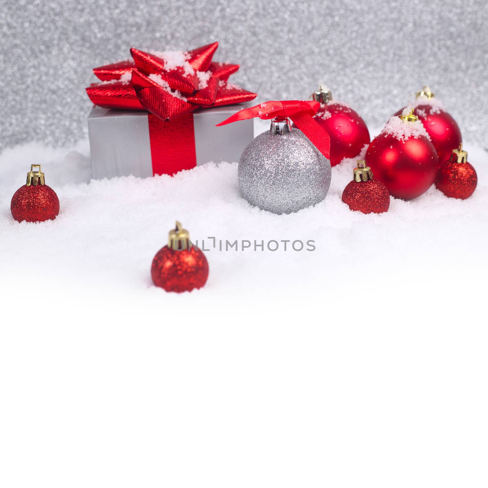 Red and silver christmas balls and gift in snow on glitter background