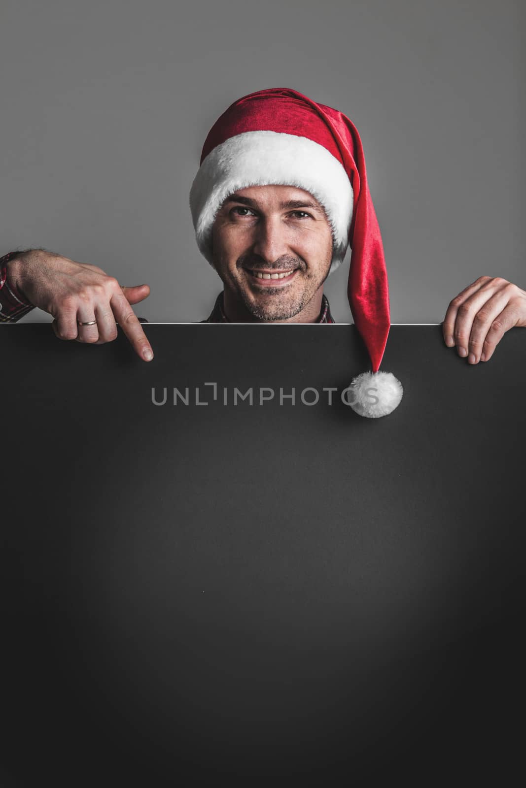 Happy smiling man in Santa's hat with black blank banner with copy space