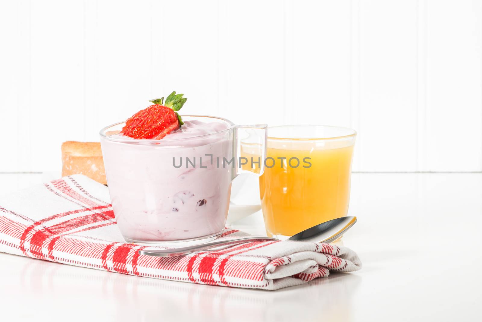 Cup of strawberry greek yogurt served with orange juice.
