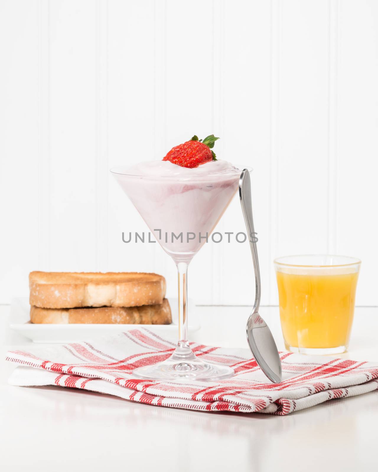 Glass filled with greek yogurt garnished with a ripe strawberry.