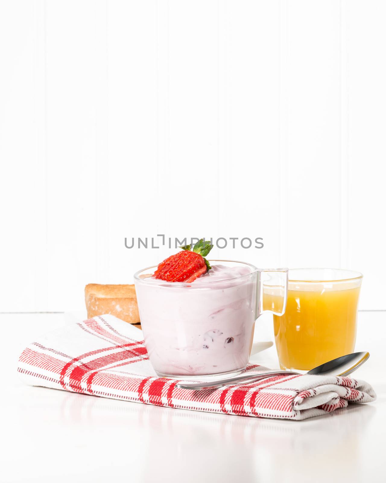 Cup of strawberry greek yogurt served with toast and orange juice.