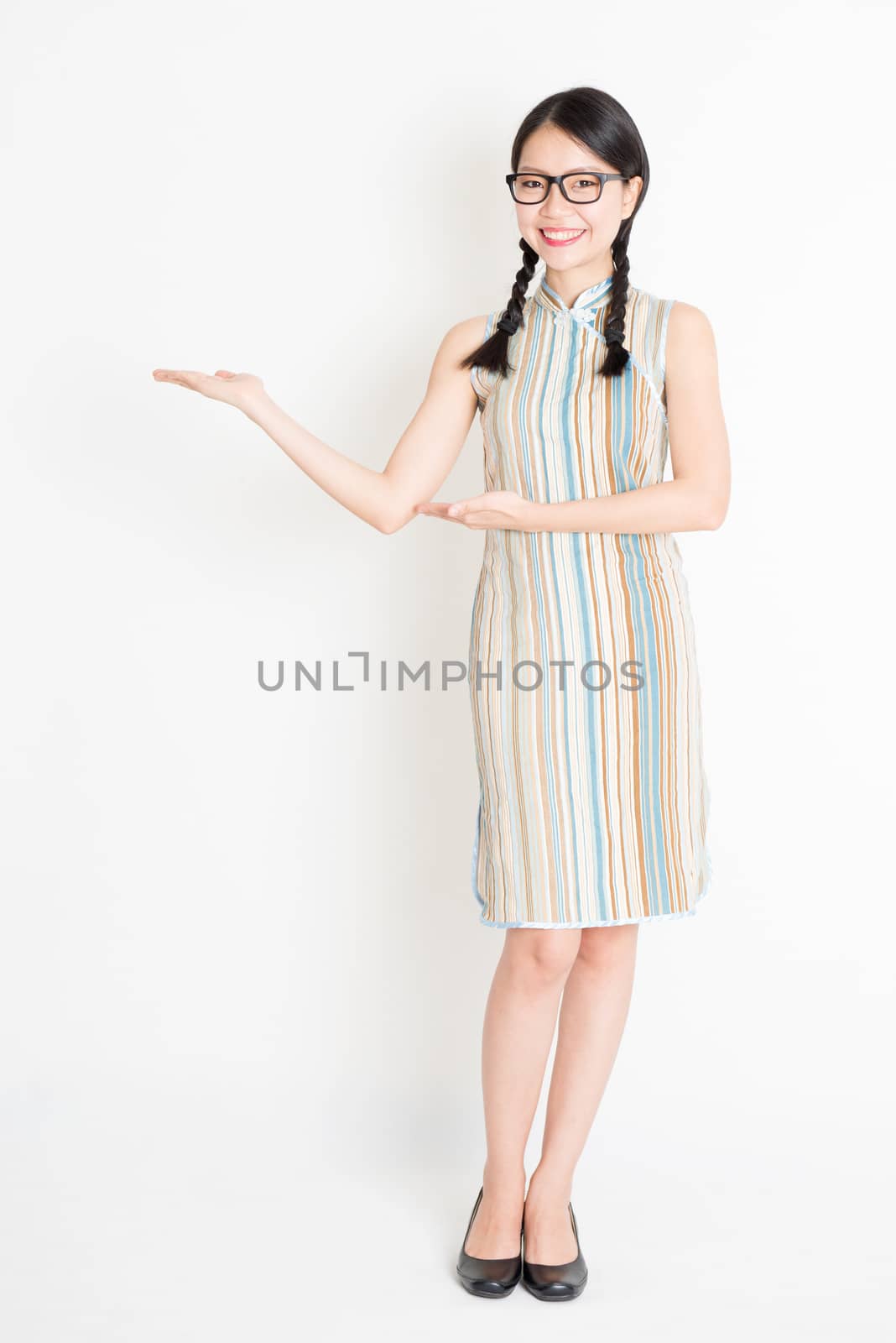 Portrait of young Asian girl in traditional qipao dress hands holding something, full length standing on plain background.