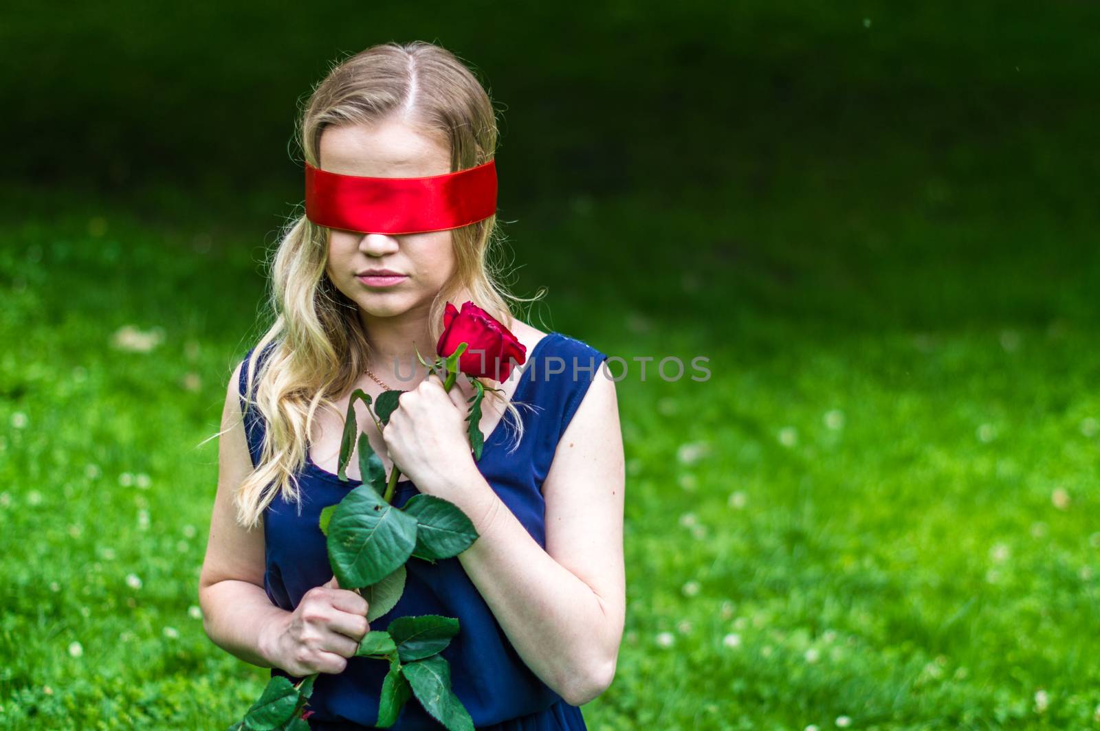 beautiful girl blindfolded holding a red rose in the park