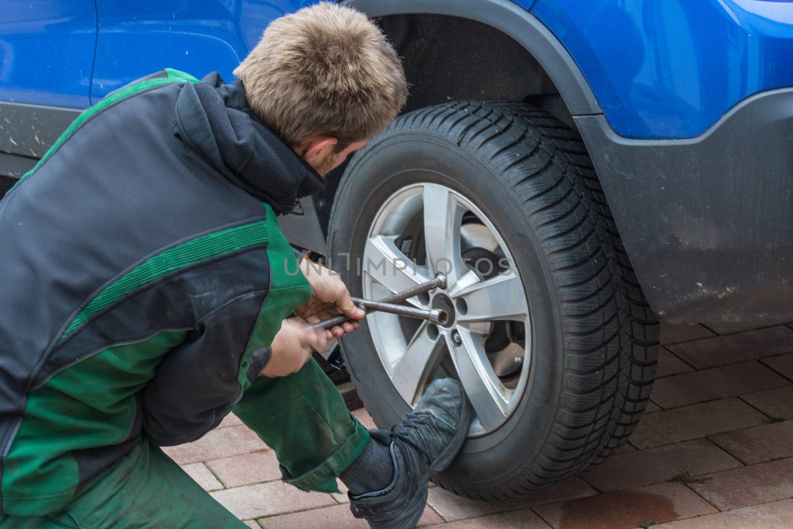 Young man  exchanging the car tires. From summer tires on winter tires on his car.