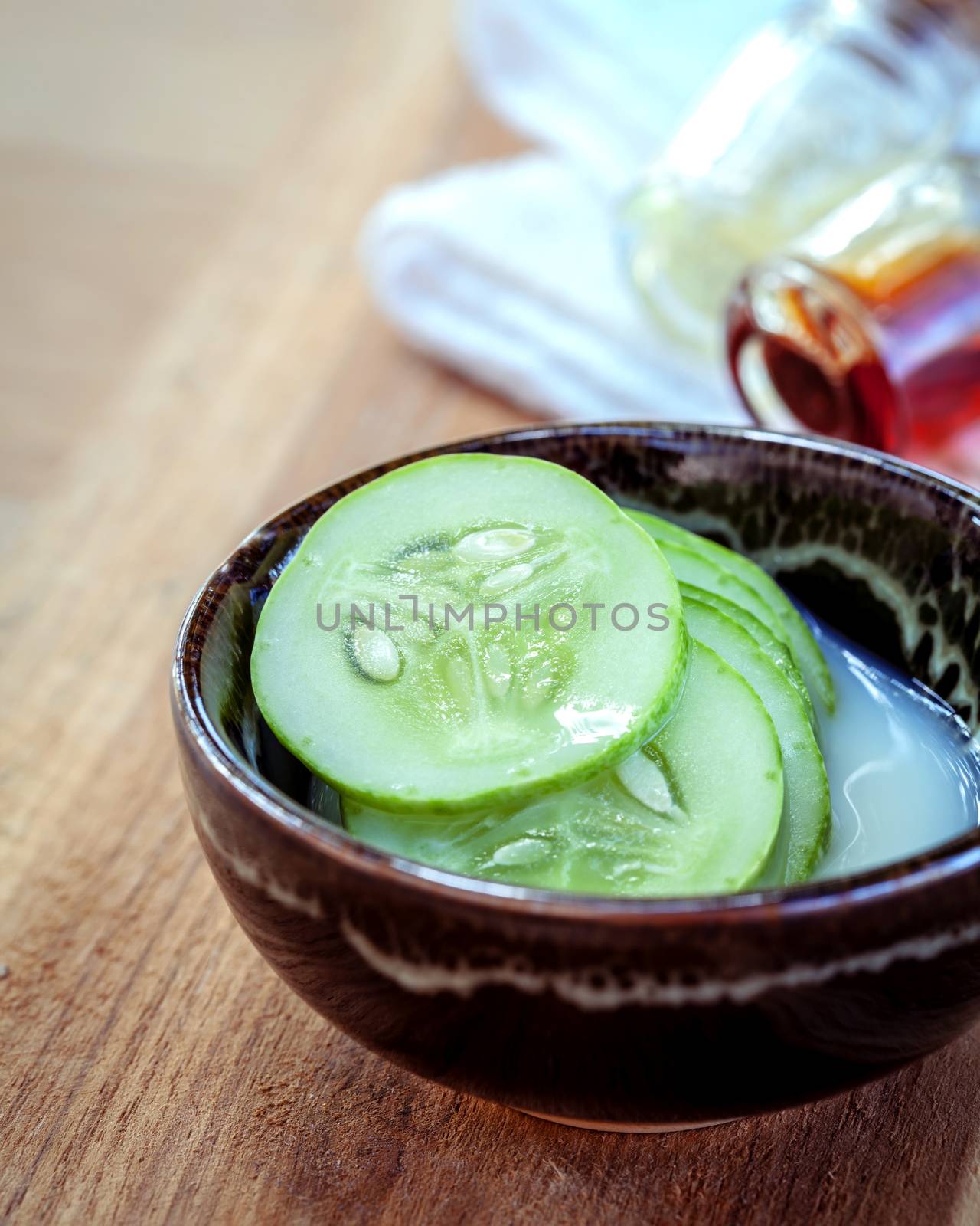 Homemade skin care and natural facial toner with natural ingredients cucumber and honey set up on wooden background. Selective focus shallow depth of field.