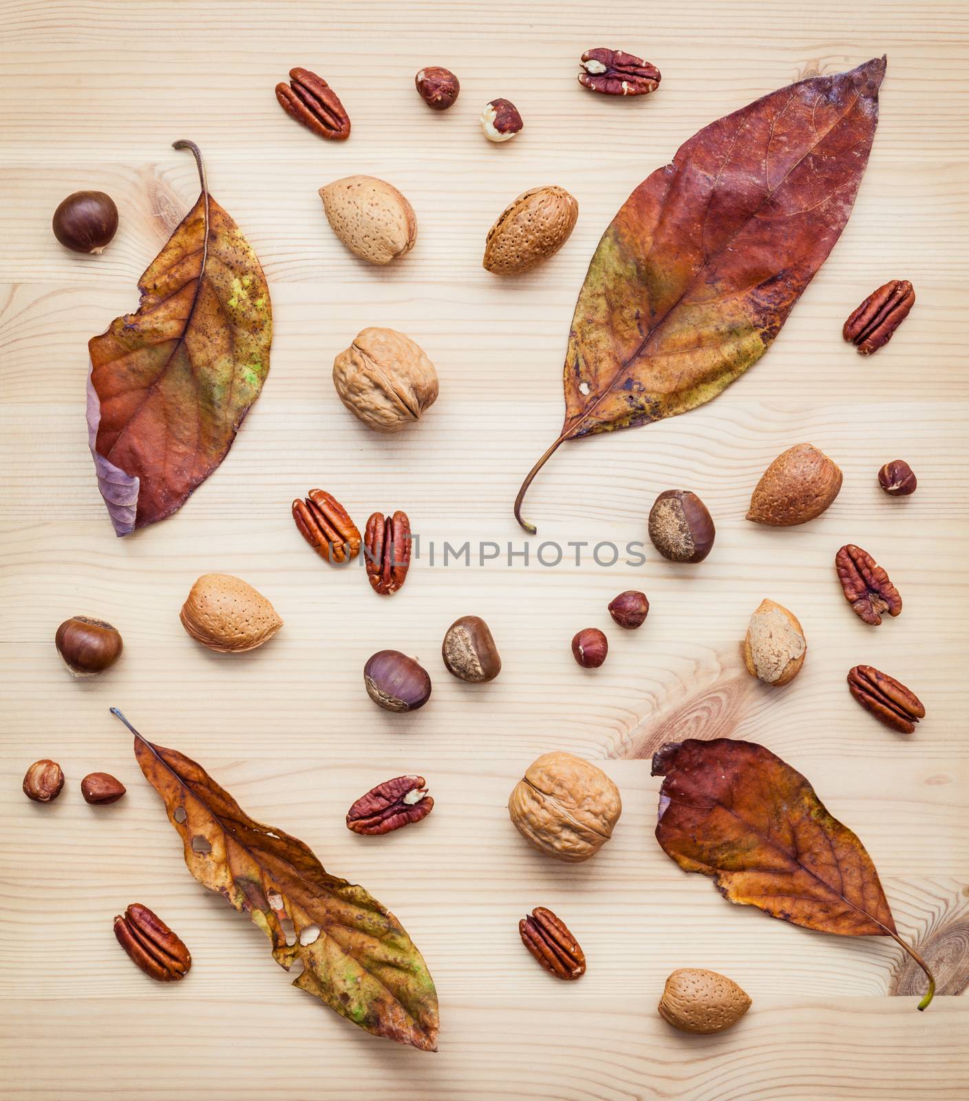 Different kinds of nuts walnuts kernels ,hazelnuts, almond kernels and pecan with dried orange leaves set up on rustic wooden background.