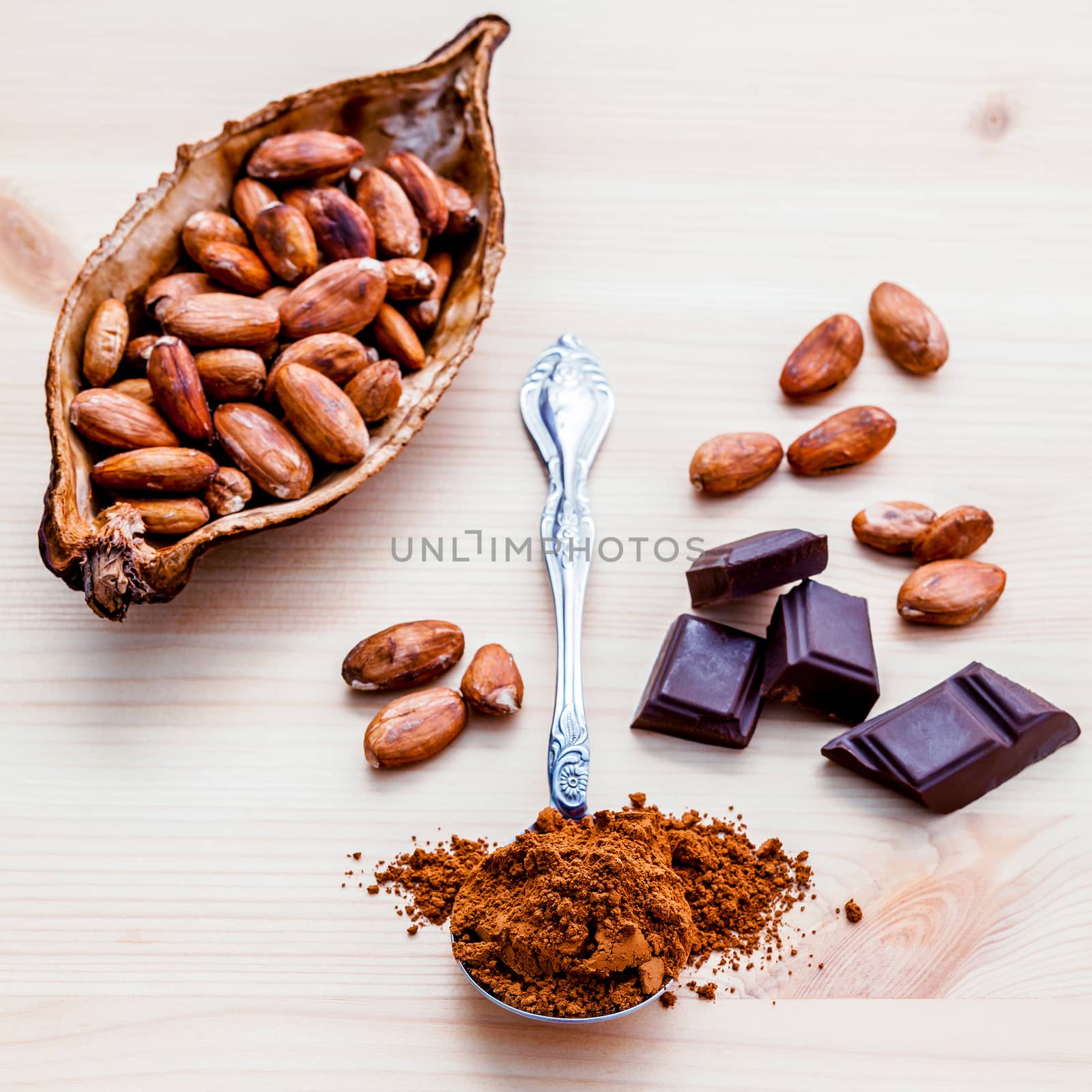 Brown chocolate powder in spoon , Roasted cocoa beans and dark chocolate setup on wooden background. Selective focus depth of field on chocolate powder.