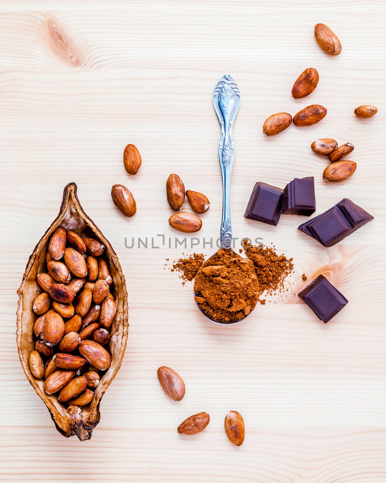 Brown chocolate powder in spoon , Roasted cocoa beans and dark chocolate setup on wooden background. 